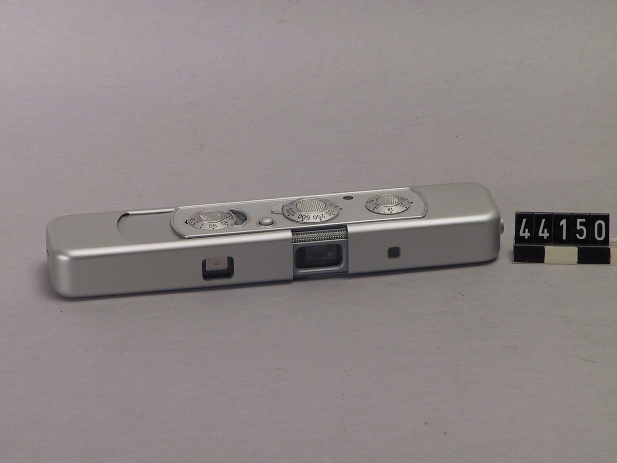 Miniatyrkamera för negativformat 8 x 11 mm, kassett för 15 eller 36 exponeringar, filmkänslighet 9-27 DIN. Filmtransport kombinerad med slutarspänning då kameran skjuts ihop och dras ut. Elektronisk lamellslutare, exponeringsautomatik 7" till 1/1000". Objektiv 1:3.5/15 mm, alltid full öppning, inställningsområde 20 cm - oändlighet. X-kontakt för blixtanslutning. Med tillhörande fodral och etui, bruksanvisning och lärobok i användning.
Tillbehör: Väska och låda.