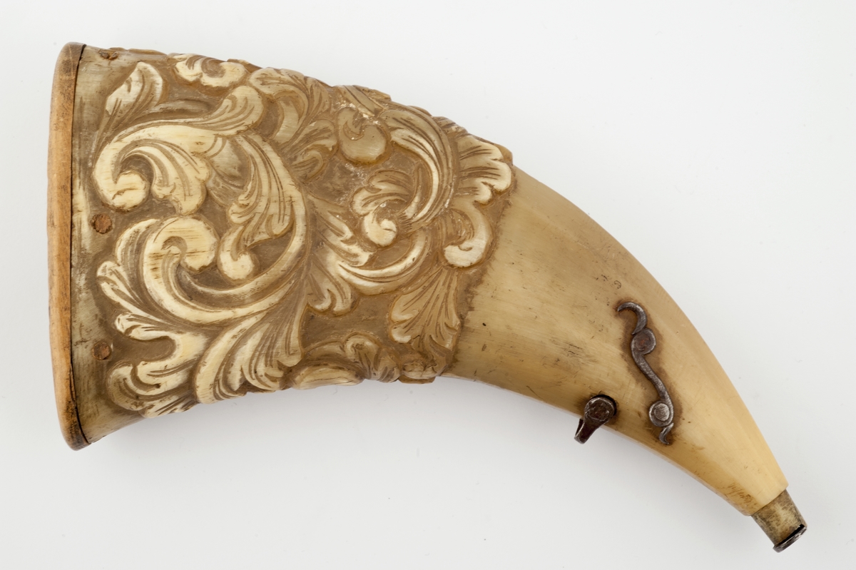 Krutthorn med bunnplate i tre med innskrift. Lukkemekanisme i jern ved munning. Ornamentikk på horn i form av akantusblader.