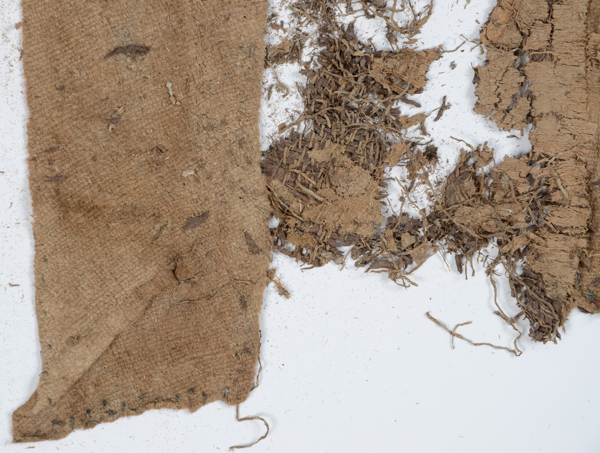 Textil.
Ca 263 textilfragment uppdelade på fyndnummer 27908:I-XII. De romerska siffrorna står för lagerföljden, d.v.s. den ordning i vilken textilen hittades, i svepask 13701.
Fnr 27908:I består av ca 15 fragment av ull vävda i tuskaft samt 2/2-kypert (fyrskaft). Beige tuskaftväv av ett ursprungligen grått garn med 11 tr z-spunnet garn per cm i ena riktningen och 14 tr s-spunnet garn per cm i andra riktningen. Fragmenten har flera originalkanter med sömmar med bevarad tråd kvar och ser ut att ha kunnat vara manschetter eller kragbitar till en skjorta eller jacka. Ett gråbeige kyperttyg har varit fastsytt på tuskafttyget. Kyperttyget är vävt av ett garn av vegetabiliska fibrer med 10 tr/cm i ena riktningen och ett ullgarn med 6 tr/cm i den andra riktningen. Ullgarnet är omväxlande grått och beige i färgen i ränder. Ovanpå det vävda lagret finns ett tunt lager vegetabiliska beige trådar.
Fnr 27908:II består av ca 62 fragment. Ett fragment är vävt i tuskaft av 10 tr z-spunnet x 8 tr s-spunnet grått garn per cm. Det har varit valkat. Övriga fragment är samma typ av 2/2-kypert som i lager I. Lager II innehåller även några mindre fragment av samma vegetabiliska väv som finns i lager XI, med ett gulgrönt korrosionsmärke på ett fragment, eventuellt efter en knapp.
Fnr 27908:III består av ca 35 fragment i 2/2-kypert (fyrskaft) av z-spunnet grått garn. Garnet är troligen av ull men väldigt sprött. En del av fragmenten har bevarade fållar.
Fnr 27908:IV består av 2 fragment i samma 2/2-kypert som i lager III. Det mindre fragmentet har en bevarad fåll.   
Fnr 27908:V består av 3 fragment i samma 2/2-kypert som i lager III. 
Fnr 27908:VI består av ca 12 fragment i samma 2/2-kypert som i lager III.  Det större fragmentet har en bevarad fåll.
Fnr 27908:VII består av 3 fragment i samma 2/2-kypert som i lager III. 
Kypertväven i lager III-VII liknar varandra.
Fnr 27908:VIII består av ca 28 fragment i kypert. Ull eller lin? Kypertväv, eventuellt samma som i lager III-VII ovan men i så fall mycket mer ihoppressad. Kan också vara samma vegetabiliska väv som i lager XI.
Fnr 27908:IX består av ca 22 fragment. 18 av fragmenten är av vitbeige ull och nålbundna (av S-spunnet tvåtrådigt garn), men 4 fragment är beigebruna och vävda.
Fnr 27908:X består av ca 54 fragment varav ca 30 fragment är nålbundna av vitbeige ull som ovan + 18 gråbeige kypertfragment + 5 beigebruna kypertfragment + 1 beigebrunt fragment i tuskaft med hål efter söm längs ena kanten. Tuskaftsväven i lager X hör troligen till en av varianterna i lager I eller II.
Fnr 27908:XI består av totalt 24 textilfragment samt 3 fragment av en knapp. Innehåller ett större fragment med stomme av brunt ullgarn, stickat eller vävt? Väv av vegetabiliska fibrer av z-spunnet garn med 9x7 tr/cm ovanpå det. 19 små tygfragment har lossnat från föremålet. Fortfarande fast på tyget sitter 13 knapphål, sydda med langettstygn av tvåtrådig beige silkestråd. Det finns också en lös rad bestående av 5 sammanhängande knapphål av samma sort som de andra. Innanför de lösa knapphålens tråd skymtar rester av tyg. Knappfragmenten består av två halvor av en metallknapp samt knappens metallögla fanns också med i fyndasken. Fyndnumret innehåller även ett band vävt i tuskaft av grått silke med 2-tr garn i varpen och 1-tr garn i inslaget, 18 dubblatr/cm samt två garndockor av 2-tr s-tvinnat grått ullgarn med tvinnat silkestråd runt.  
Fnr 27908:XII består av 4 slätstickade ullfragment, varav två är rundstickade av dels ljust och dels grått garn i randning, 1-tr s-tvinnat med 2 maskor/cm och 2 varv/cm. Lagret innehåller även 3 hårdare små fragment av oklart material.