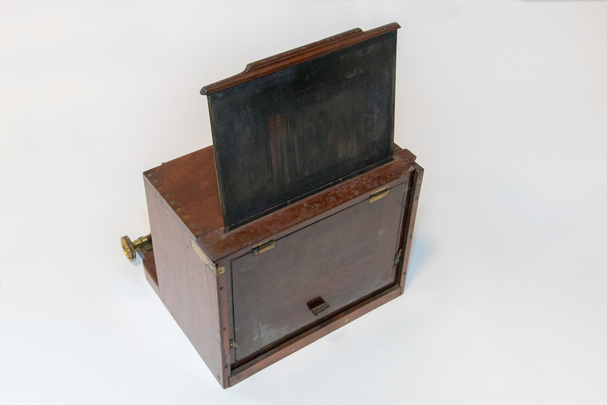 Gruppering med fotokamera i oppbevaringskasse, separat metall-lokk, stereolinse, lause delar som negativplate, mattskive, blendarsett og diverse smådelar.