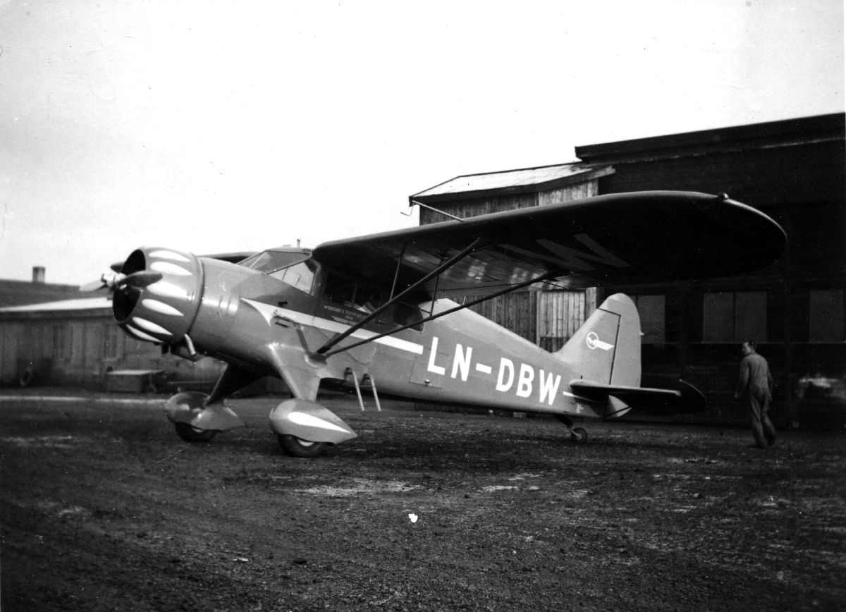 En C5 Polar fra Widerøe parkert foran hangar, med en person på inspeksjonstur rundt flyet.