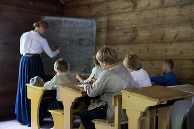 Children at their desks in the old school house while teacher writes at the black board. Foto/Photo