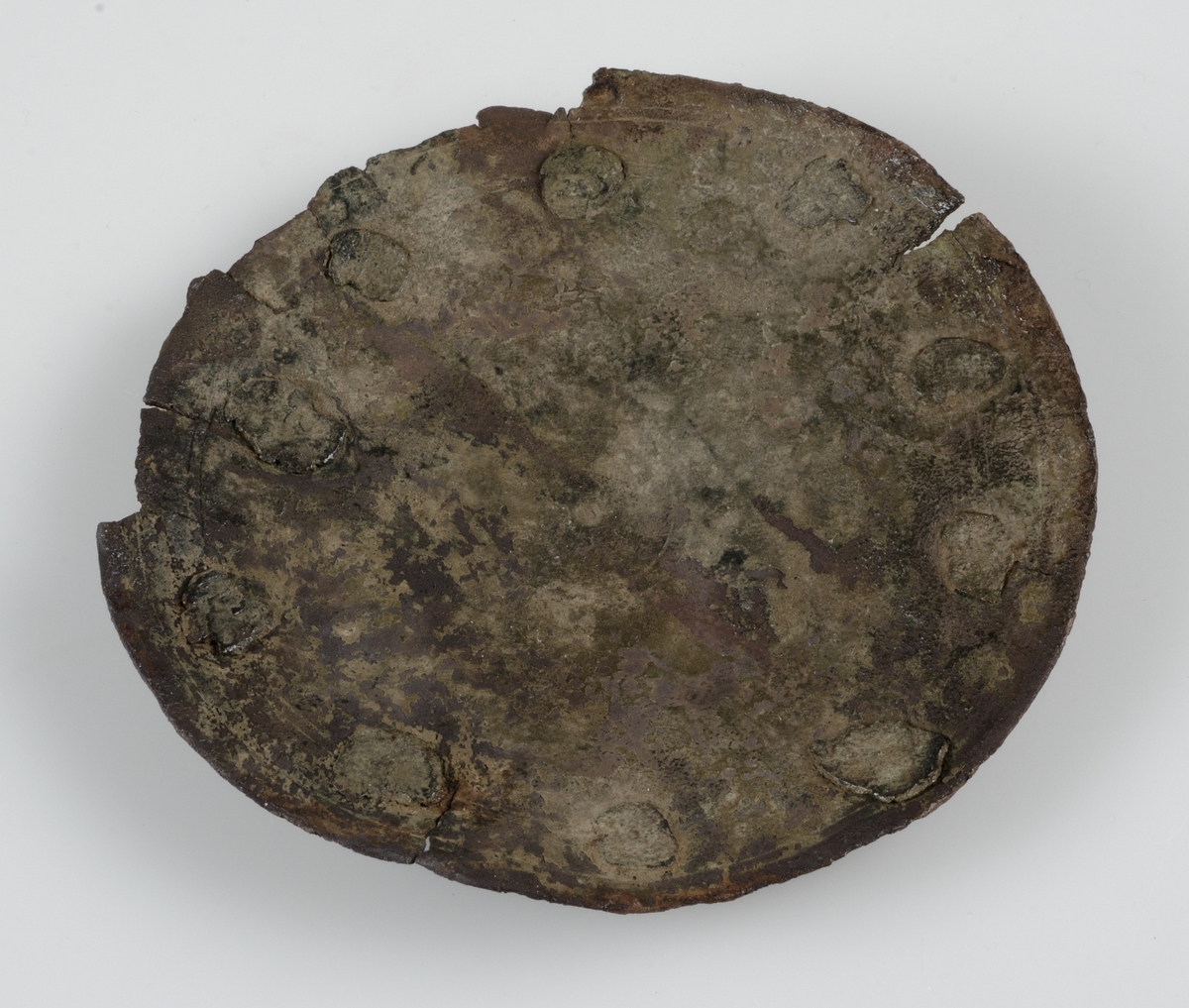 Del av kanna i brons. Cirkelrund med 11 nitar i kanterna. Svagt välvd. Trolig datering tidig islamisk tid, cirka 640-900 enligt vår tideräkning.