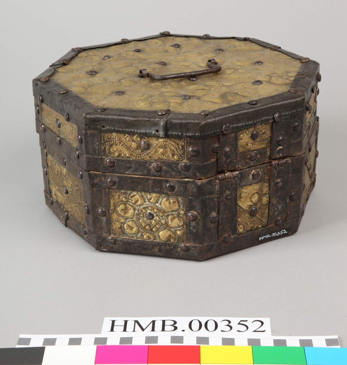 Åttekantet. Den har dekorerte flater i messing med jernbeslag og det hele er naglet på tre. På lokket er det en hank. Flaskefôret er låsbart, men den originale nøkkel mangler.