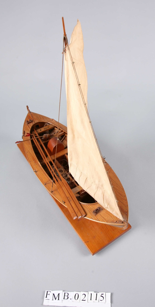 Modellbåt med mast og to seil. Den har 3 årer, 2 bøyer, et garn og en dregg.