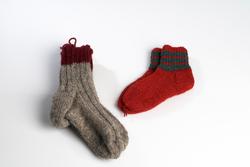 Sokker i ull. Ene sokken er strikket med grått og rødt garn.