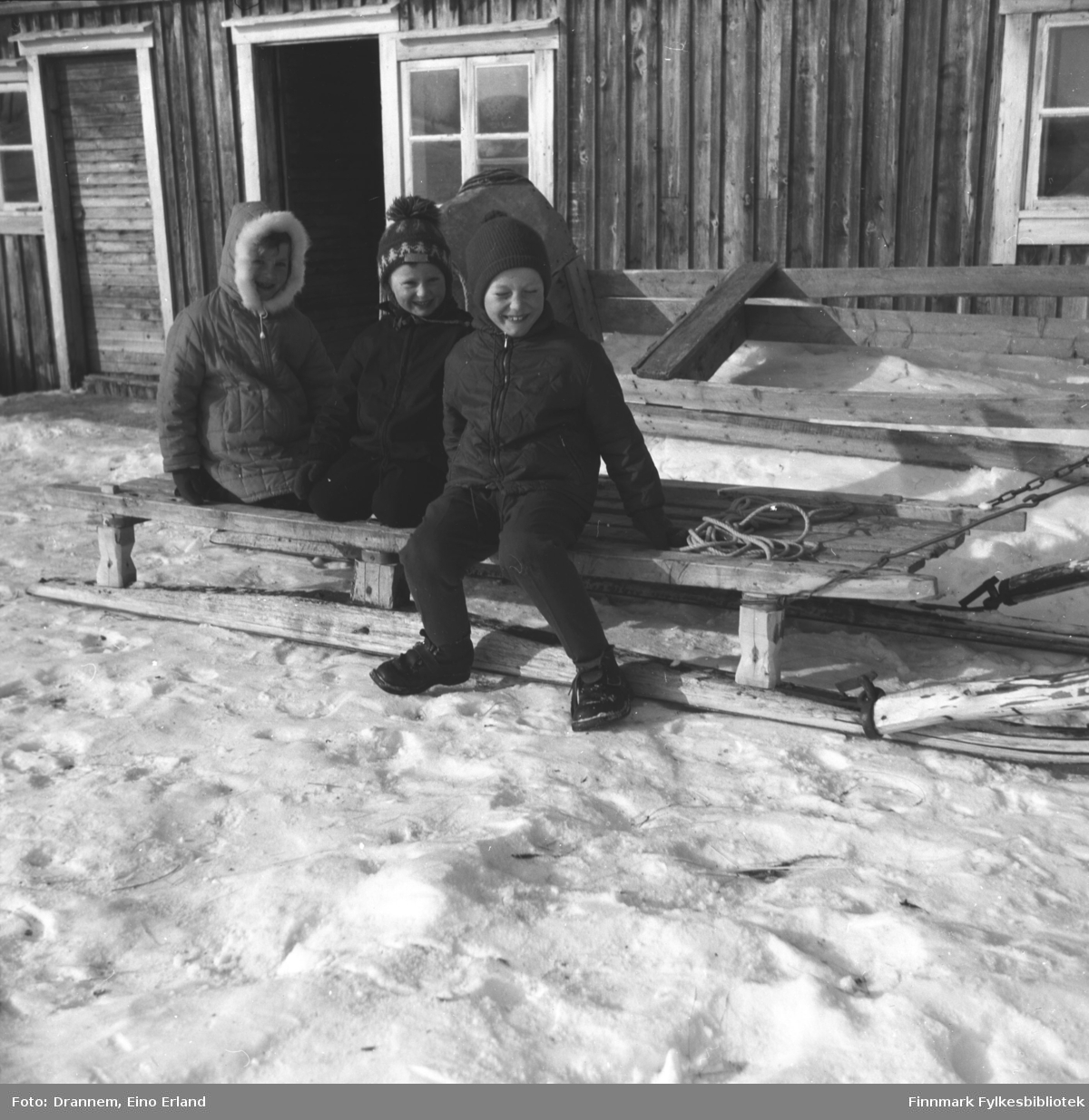 Tre barn sitter på en slede utenfor en bygning. De er fra venstre: Kari, Hans og Ole Gabrielsen.