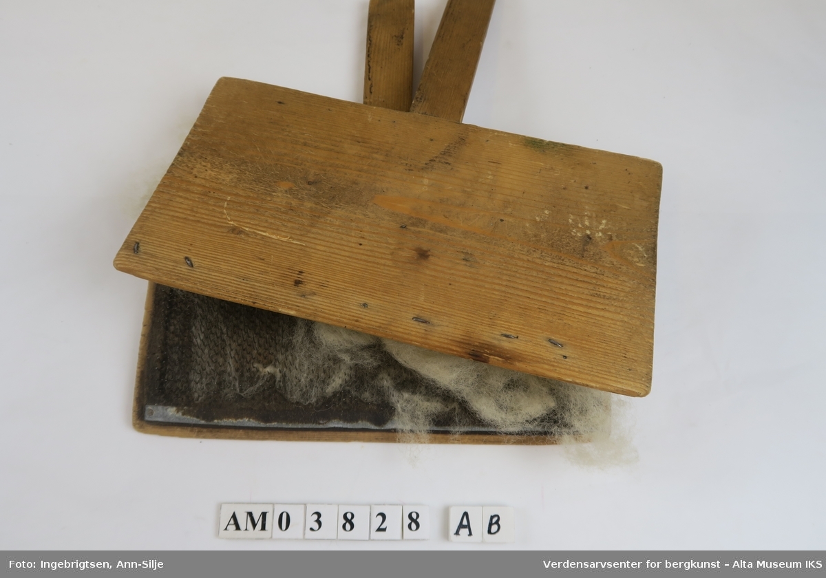 To rektangulære treplater med lærplater som er fylt med metallpigger. Dette blir brukt til å karde ull. I mellom platene er det fortsatt en stor dott med ull.