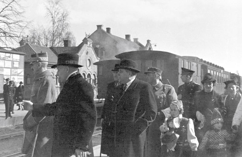 Hambro, fylkesmann Knut Nordanger og politimester Reidar Beichmann tar imot kongefamilien på Hamar stasjon.