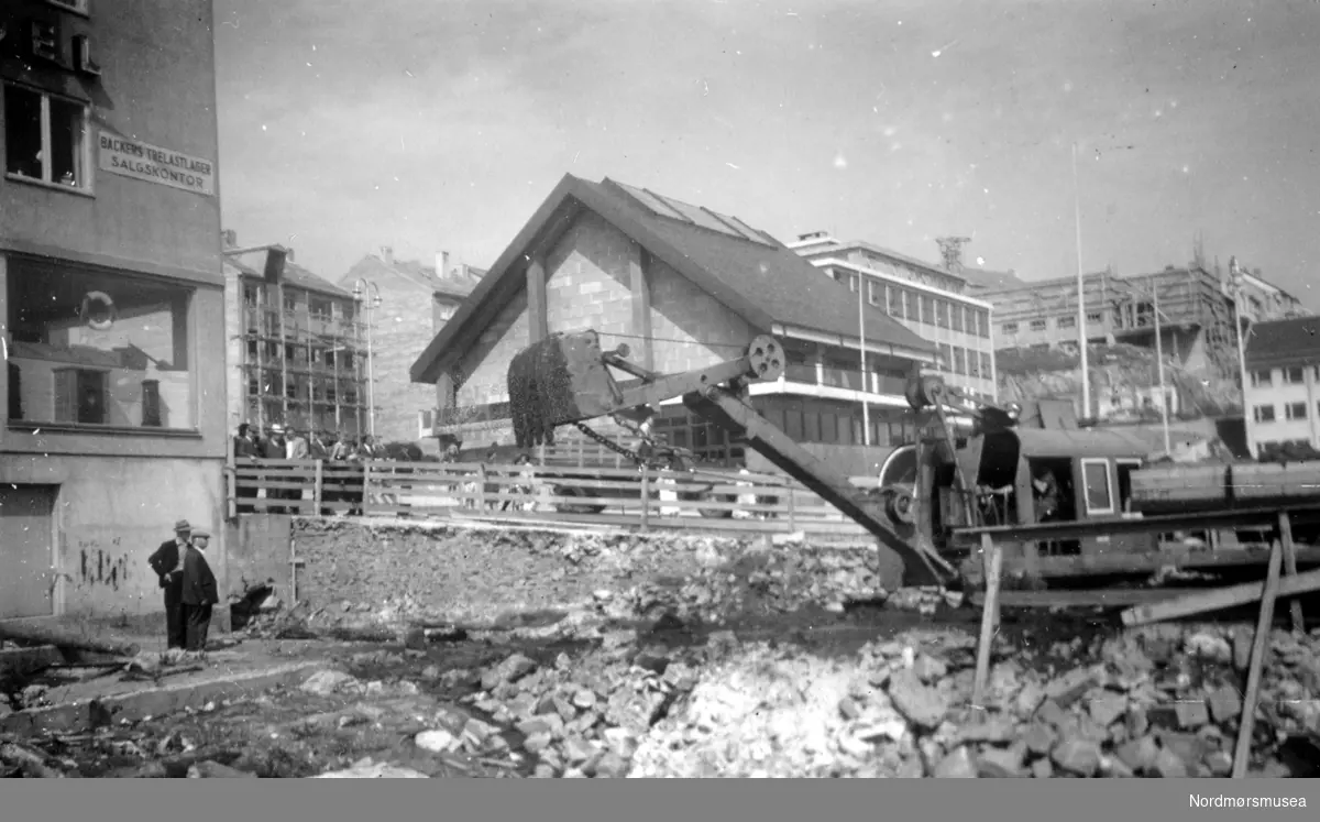 På bildet ser vi "Entreprenør Svendsvik & Sønn" sin store gravemaskin, som graver opp tomten til Havnevesenets nye bygg i Kaibakken 1 på Kirkelandet i Kristiansund. Havnevesenets nye bygg vil ligge omtrent på samme grunn som det gamle havnekontoret. I bakgrunnen ser vi det nye Rådhuset i Kaibakken 2, som ble sluttført i dette året. Til venstre ser vi Berge A/S's nybygg. Bildet er datert Juni 1953, og er fotografert fra sør. Se også bilde 1953/1466 (KMb-1953-000.1466.jpg). Skilt Backers trelastlager. Hotell Fosna under bygging bak til høyre. Nordmøre museums fotosamling.

I dag er vi i året 1953 og befinner oss nederst i Kaibakken hvor nysgjerrige tilskuere ser på den store gravemaskinen til "Entreprenør Svendsvik & Sønn" som graver opp tomten til Havnevesenets nye bygg i Kaibakken 1, hvor senere blant annet “Onkel” og nå “Havnekontoret” har tilhold. (2022) Bygget ble ferdig i slutten av 1954 og følgende flyttet inn i tur og orden: Ellingsen Sko, Anton Tolås, Algea Produkter, Havne og Loskontoret, Andr. Lie, Arne Lund & Sønner, Ulrik Olsen AS, Sjømannskontoret, Gabriel Slørdahl jernvareutsalg,  Det Kommunale Sundbåtvesen, Wolland & Dyrlie og til slutt byggherren Havnevesenet som innvier sitt nybygg 26.01.55. I bakgrunnen ser vi det nye Rådhuset i Kaibakken 2, som ble sluttført i dette året. Til venstre har vi Reidar Berges bygg i Kaibakken 3 med salgskontor for Backers trelastlager AS. Til venstre for rådhuset ser vi Tangengården med stillas på fasaden. Hotel Bondeheimen under bygging bak til høyre, mønsås 09.08.1953. Husfliden flyttet inn i bygget mot syd (senere Intim) den 04.12.1954, Kaffistova åpnet 05.02.1955 og Hotel Bondeheimen åpnet dørene 14.02.1955. Kilde: Kai Helge Andersen