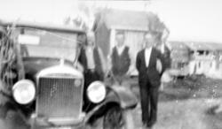 uklart bilde av tre menn ved siden av en bil. I bakgrunnen s