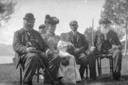 Tre mann, en kvinne og to barn, sittende. Mannen til venstre