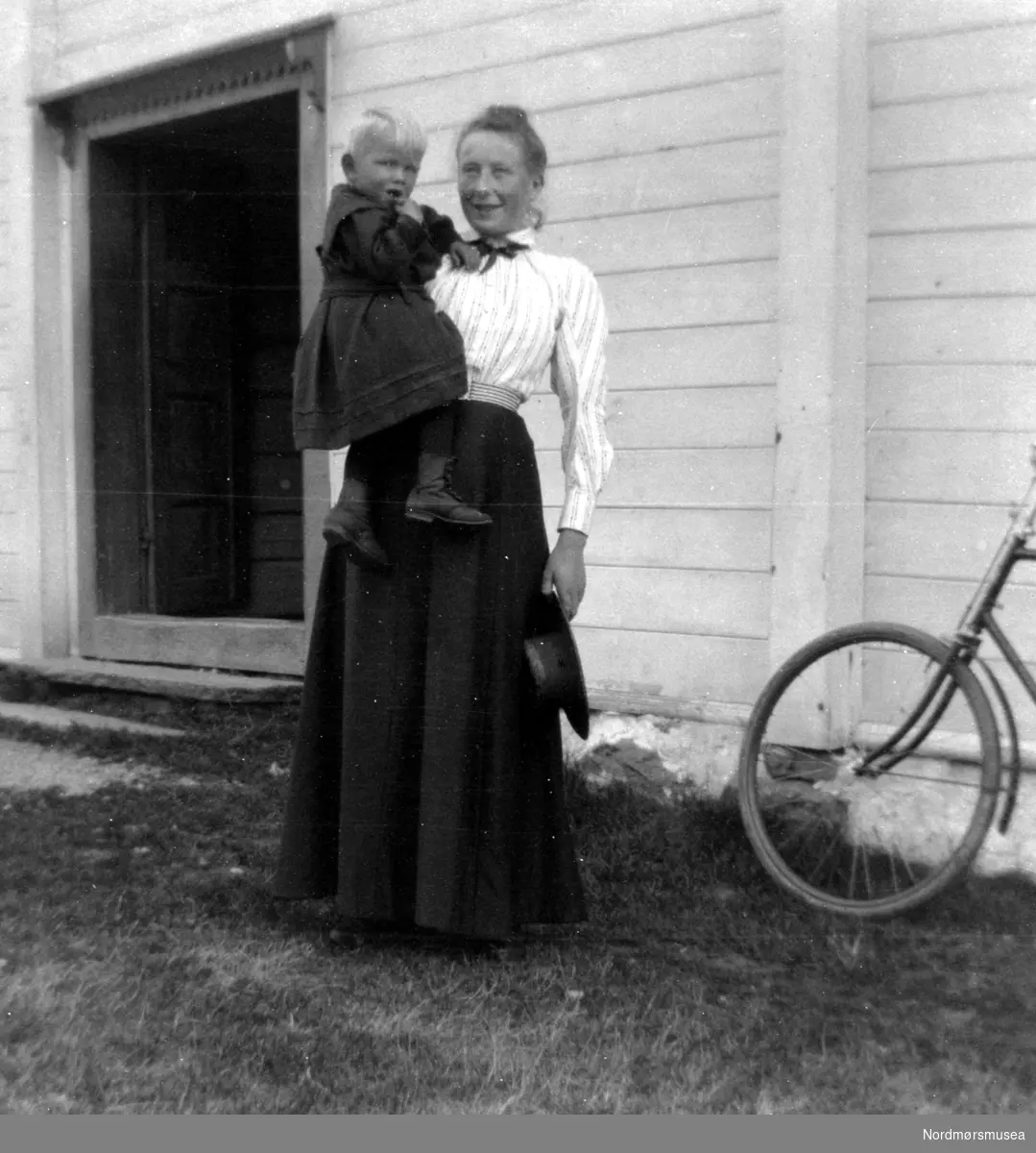 Foto av en mor med barnet sitt på armen. Det er ukjent hvem vi ser på bildet, samt hvor og når bildet er tatt. Fra Nordmøre Museums fotosamlinger. serie
