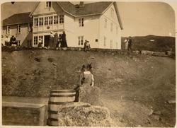 Mennesker utenfor et større hus. Fra et album med skadde bil