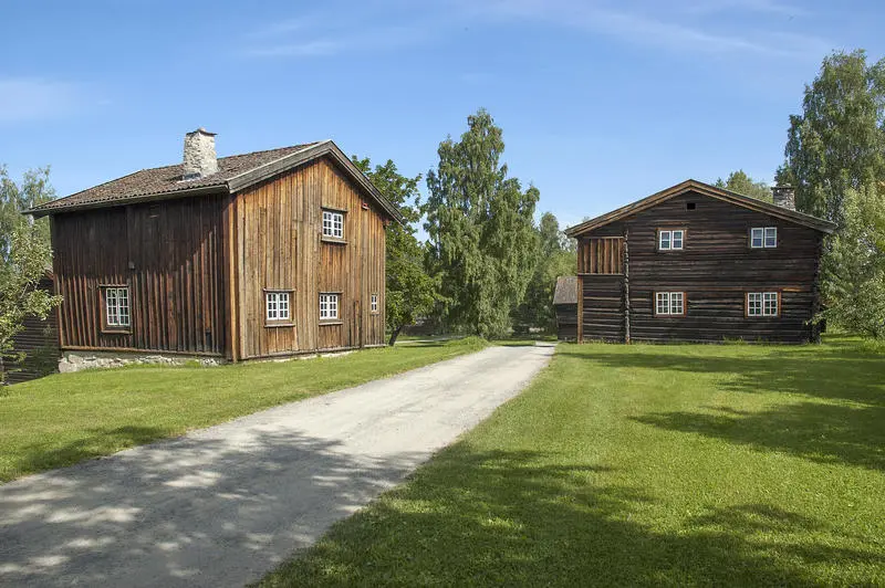 Grusveg som leder inn mellom to brunlige tømmerhus i to etasjer.