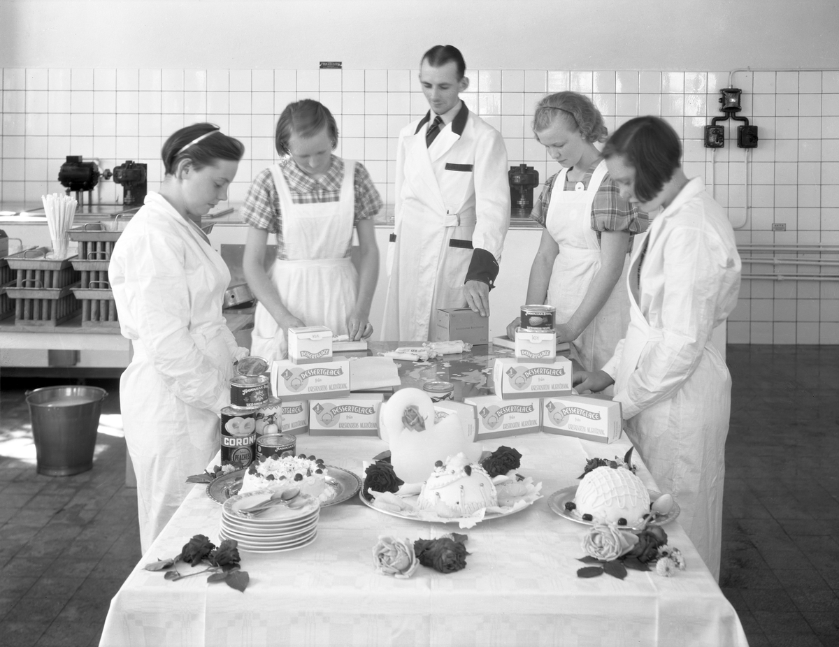 Arbetsklädda kvinnor och man vid bord med glassprodukter.
Fotografens ant: Karlstadsortens - Mejeriförening.