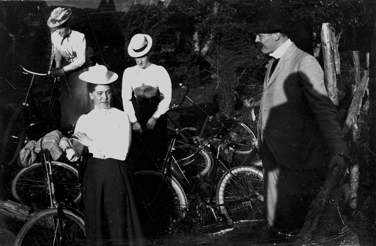Tre kvinnor och en man med cyklar, år 1900. Fotograf Alfred Bergendahl. Givare H Bergendahl.