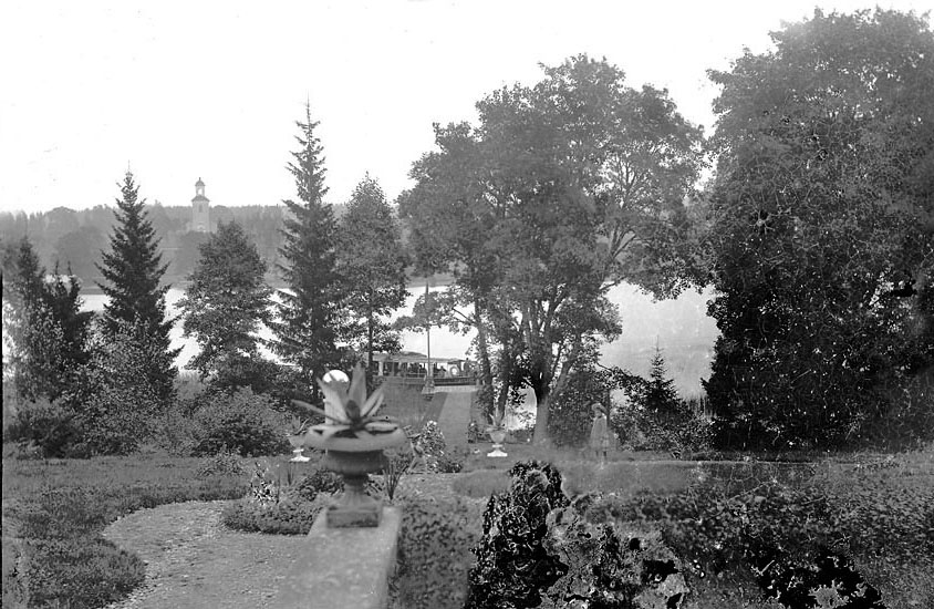 Asa Herrgård, parken, med Asasjön och Asa kyrka i bakgrunden, ca 1890-tal. En ångbåt har lagt till vid bryggan.