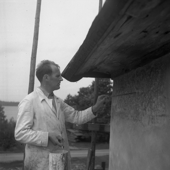 Konservator Wahlgren restaurerar en (yttre) kalkmålning på fasaden till Sjösås gamla kyrka. 1943.