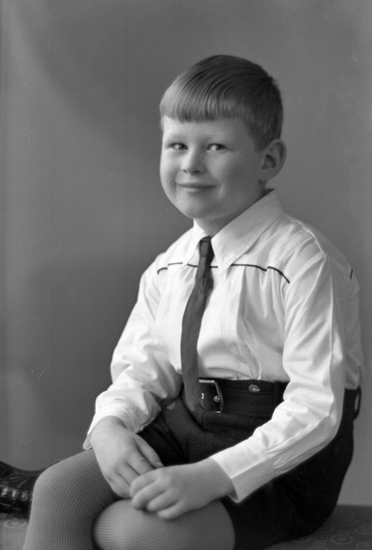 Foto av en okänd pojke i skjorta, slips och kortbyxor.
Knäbild. Ateljéfoto.