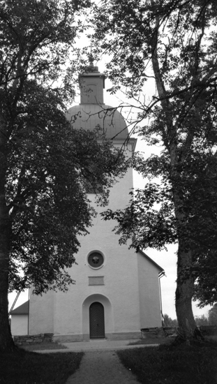 Foto på en kyrka framifrån med träd jämte.