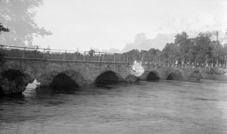 Foto på en landsvägsbro med vatten under och två cyklister på bron.