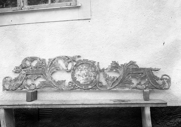 Foto av kyrkliga inredningsdetaljer på en bänk utanför kyrkan.