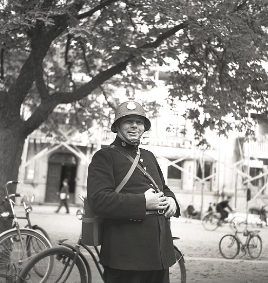 Luftskyddsövningen, 1941. 
En glad polis i hjälm m.m. utanför dåv. poliskontoret på Kronobergsgatan. 
I bakgrunden skymtar dåv. fastigheten på kv. Lejonet 3. Enligt kommentar är polisen Axel Nordström (1902-1978), Växjö.