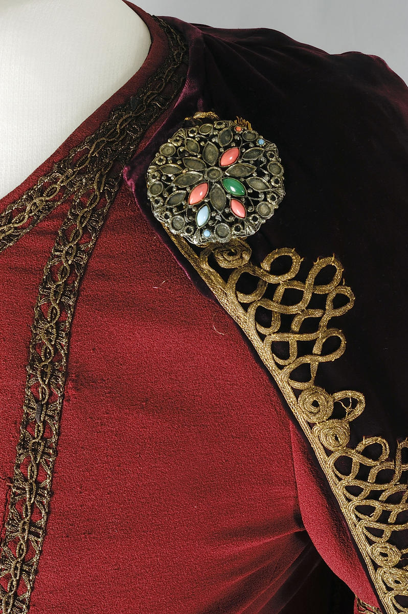Close up picture of the details in the costume of Isolde. A red dress with gold details and the picture shows the brooch that attaches the cape to shoulder of the dress.