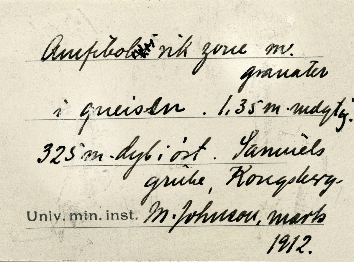 Tekst på etikett i eske:

Amfibol rik zone m. granater i gneisen. 1,35 m mægtig.
325 m. dyb i øst. Samuels grube, Kongsberg.
M. Johnson, marts 1912.

+ papirlapp