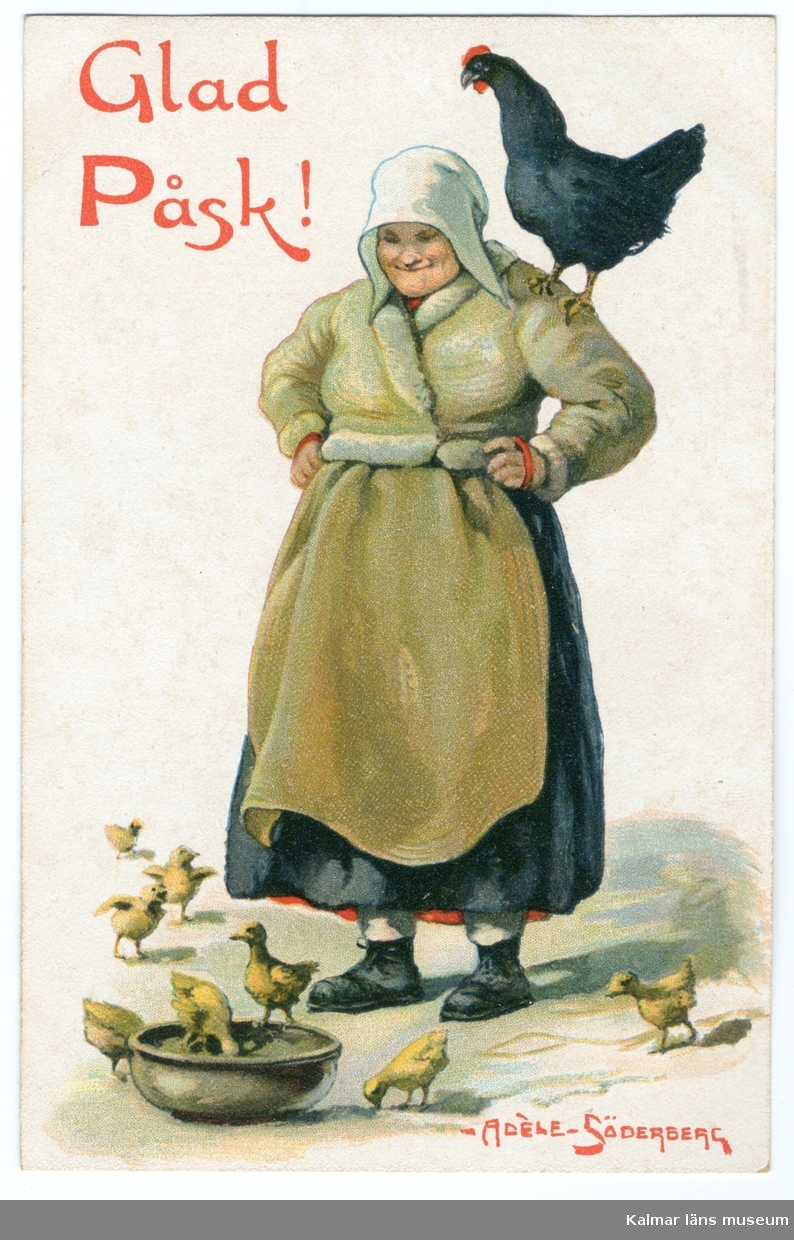 En kvinna står med händerna i sidorna och tittar på kycklingar som äter ur en skål som står på marken. På hennes ena arm sitter en svart höna.