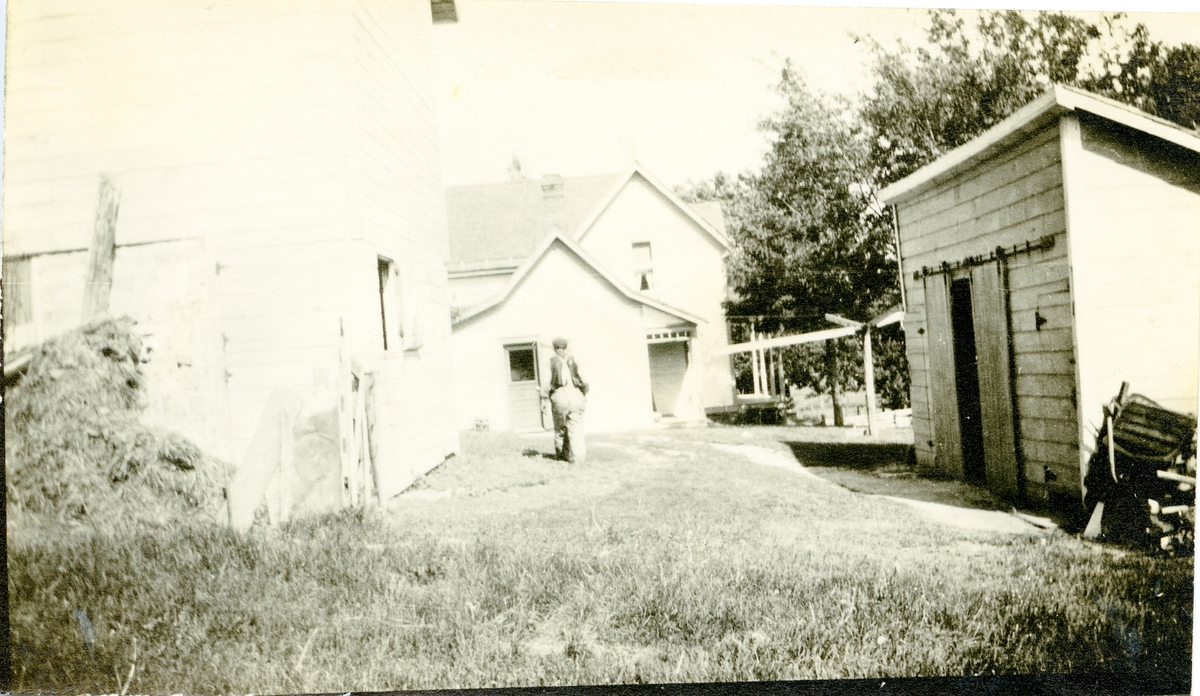 Bildet viser et tun med to hus og en garasje. En mann går over gresset mellom disse bygningene. I Amerika.
