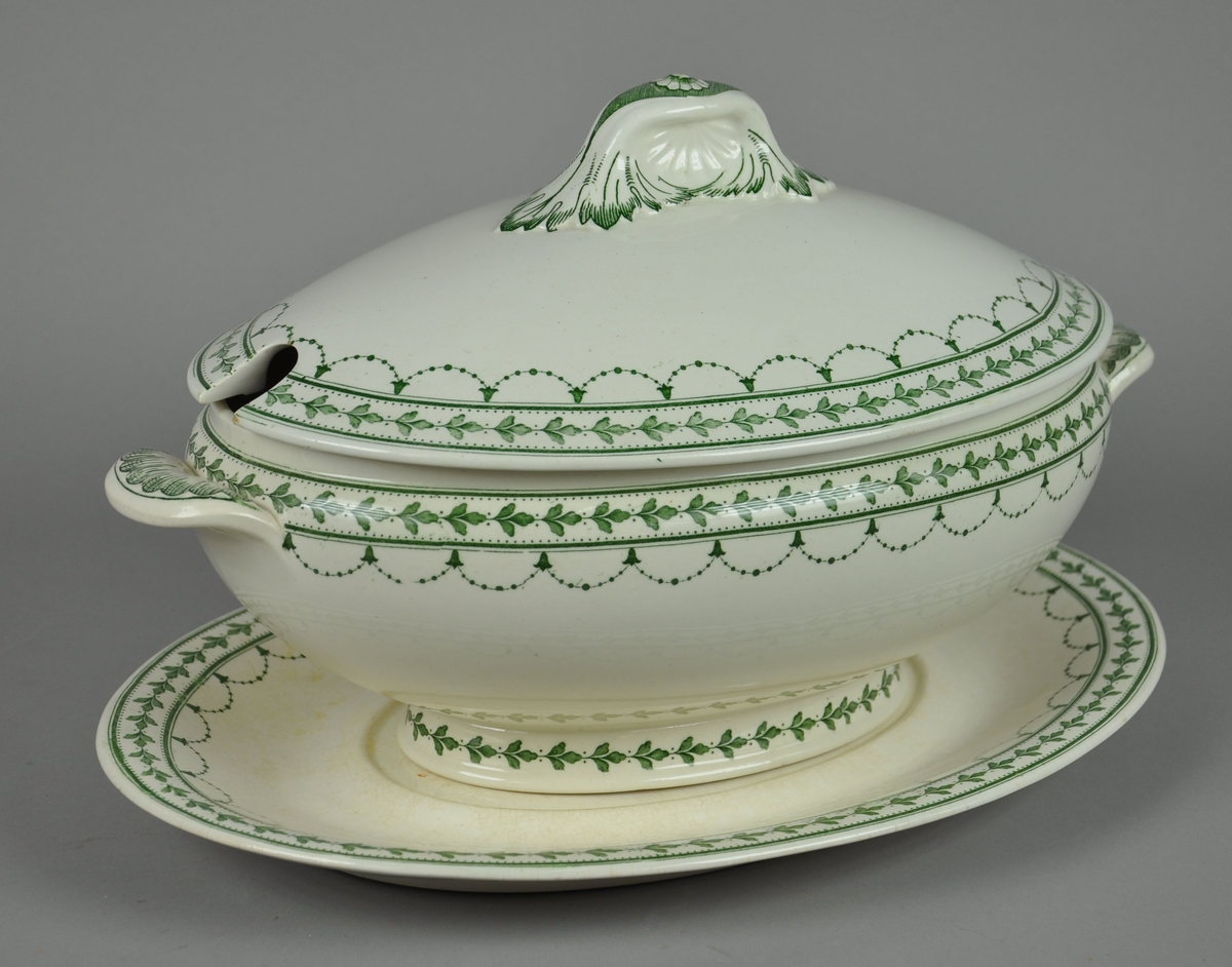 Ovalt lokkfat med tilhørende lokk og løst underfat.  Fatet har to håndtak. Det er av keramikk, steingods, med grønn bord. Borden består av eikekrans og guirlandere. Mønsteret heter Fontainebleau.