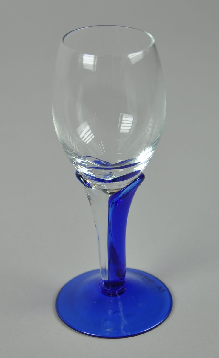 Drammeglass med stett. Glasset har en oval eggeform. Sokkelen er helt blå, mens stetten er sammenformet av to glass hvor den ene typen er klar, og den andre er blå.