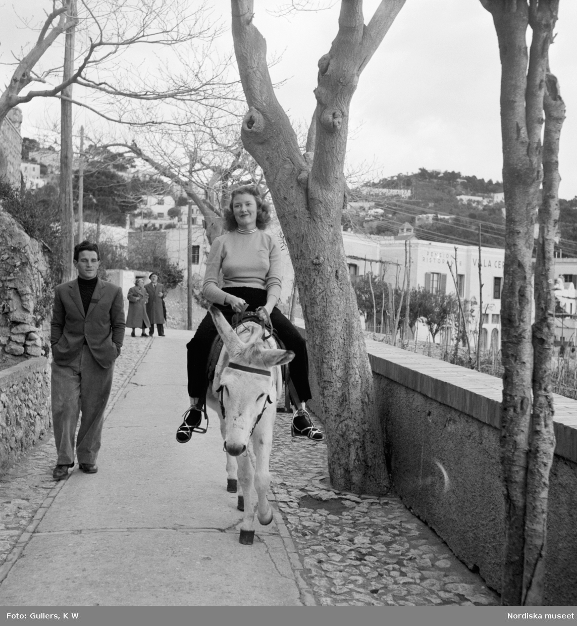 En flicka som rider på en åsna och en man går bredvid med händerna i byxfickorna