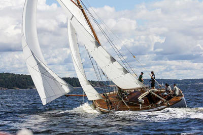 Skøyta S/Y Venus i vannet, tre seil, fire personer ombord. I bakgrunnen utsikt til skog.. Foto/Photo