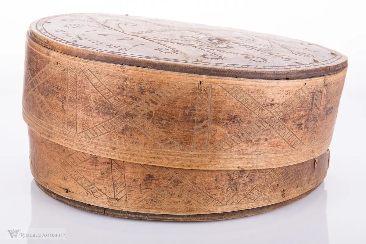 Eit kvistmønster/bregner på lokk. Skravert kryss- mønster langs trosken. Rosett av spetter i bunnen.