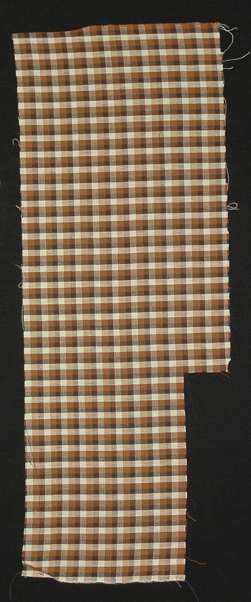 Bomullstyg till klänning, 29 x 77 cm (en bit urklippt), tuskaft, smårutigt i svart, brunt och vitt.

Katalogiserad av Karin Nordenfelt, Elisabet Stavenow,
Marie-Louise Wulfcrona-Dagel.