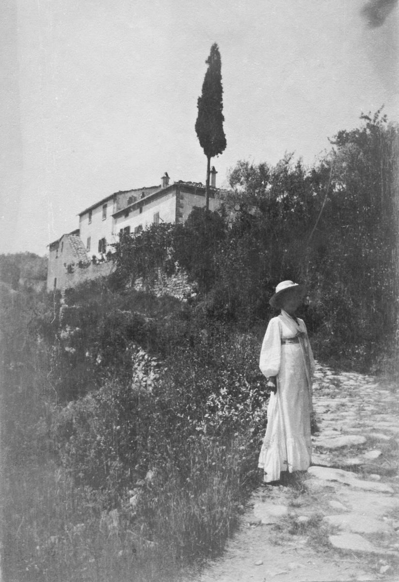 Ester Ellqvist-Bauer i Italien. Hon står på en stenlagd väg upp mot ett bostadshus.