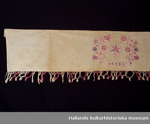 Hängkläde av bomull och linne. Knuten frans i rosa och vitt. Broderier i rosa och blått bomullsgarn. Märkt: M G E D ÅR, 1845.
