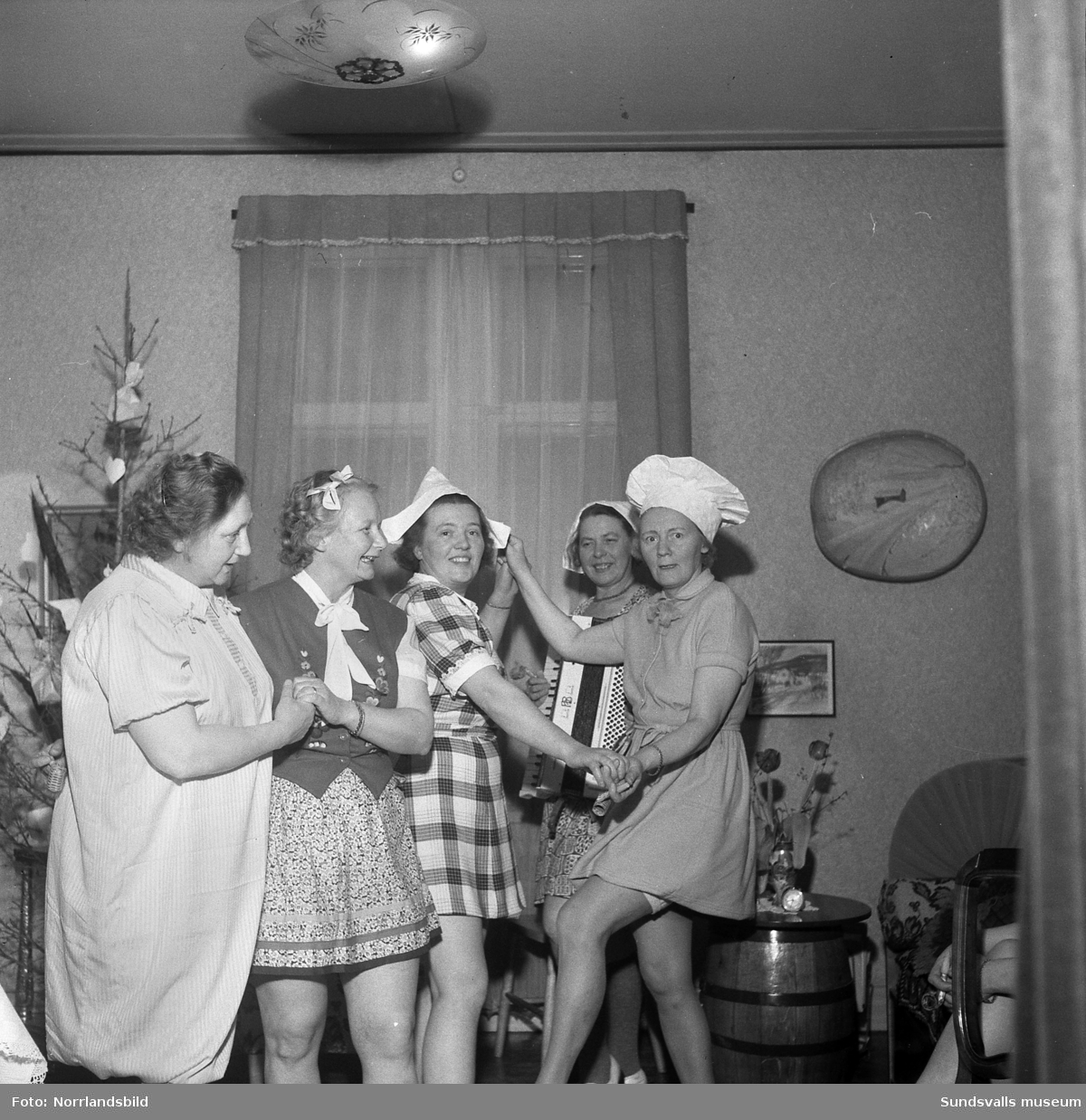 Humoristisk julgransplundring med sex glada damer i en syjunta (Fredriksson). En av kvinnorna spelar dragspel.