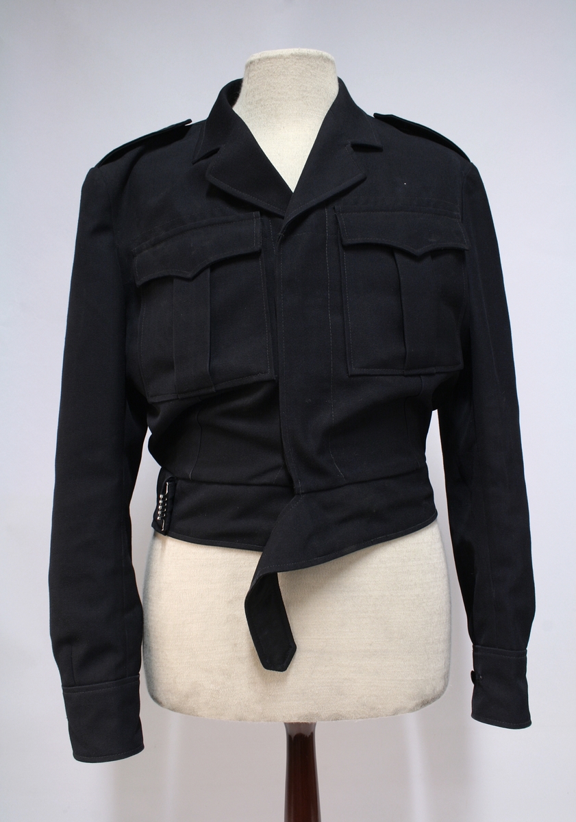 Battleuniform med bukse, skjorte, slips, bandolær. 

Kortet er tidligere utstilling og ikke en del av uniformen.