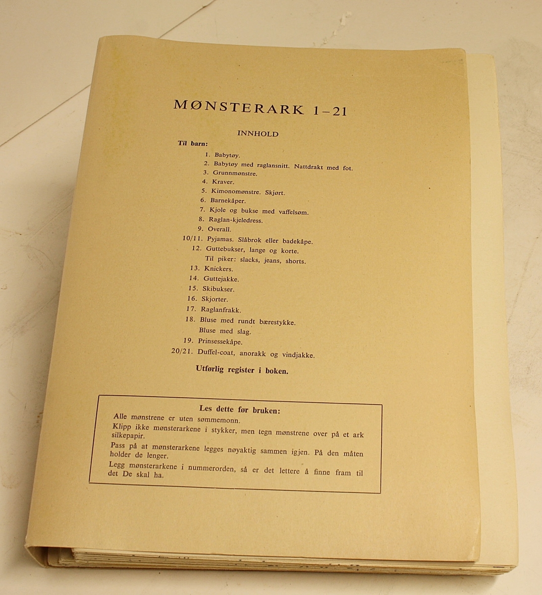 Rektangulær, stående koffert. Lokk, håndtak og lås. Innhold: "Den Store Norske Syboken" Dovre Mønster. Forfatter: Ella Lund. To holdere med mønsterark (1-21 og 22-42).