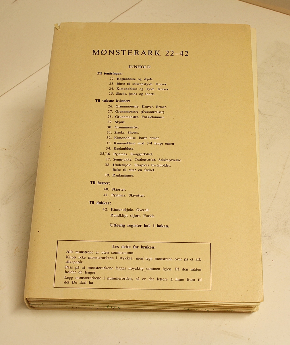 Rektangulær, stående koffert. Lokk, håndtak og lås. Innhold: "Den Store Norske Syboken" Dovre Mønster. Forfatter: Ella Lund. To holdere med mønsterark (1-21 og 22-42).