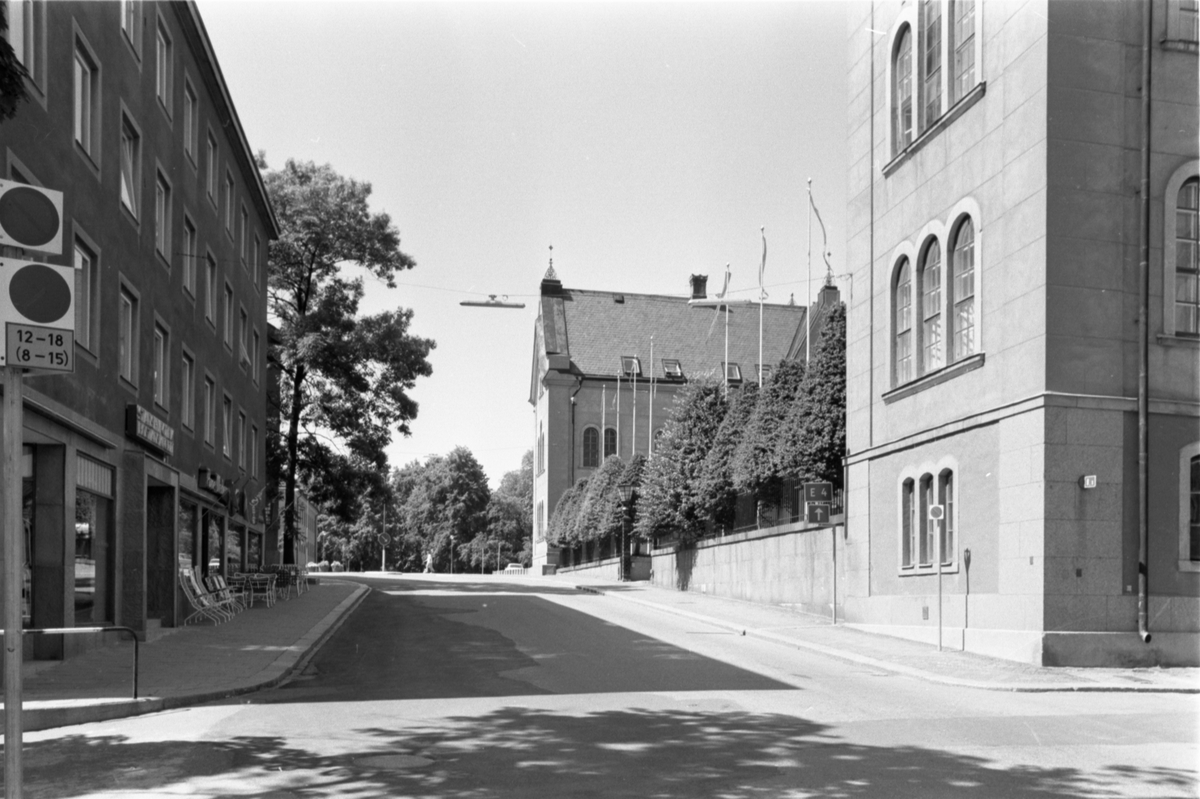 Storgatan mot väst från Läroverksgatan. Till höger lligger stadshuset, med flera flaggstänger med vimplar och konformklippta buskar. Utanför byggnaden till vänster står bord och stolar uppställda.
Stadshuset. År 1859 fastställdes att en ny skola skulle uppföras på Cederhielmska tomten. Arkitekt var Johan Fredrik Åbom, byggmästare Jonas Jonsson. Byggnadsarbetena påbörjades 1860 och invigningen av läroverket skedde år 1864. Läroverk fram till 1914. Byggnaden användes för militära uppgifter under krigsåren. Efter en ombyggnation 1921, av Axel Brunskog efter skisser av byggnadsingenjören Iwar Olsson, blev huset ett stadshus. Interiören förändrades mest då kakelugnar byttes ut mot centralvärme. Ytterligare en betydande upprustning av interiören gjordes på 1990-talet.