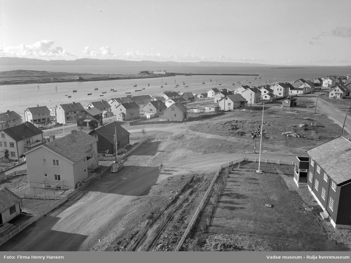 Vadsø 1957. Bildet er tatt fra kirken (som sto ferdig i 1958). Bildet viser boliger langs Damsveien og Nyborgveien. Til høyre og nærmest kamera vises en del av presteboligen. På havna ligger mange båter. Vi ser en del av øya med Vadsø sildoljefabrikk og moloen.