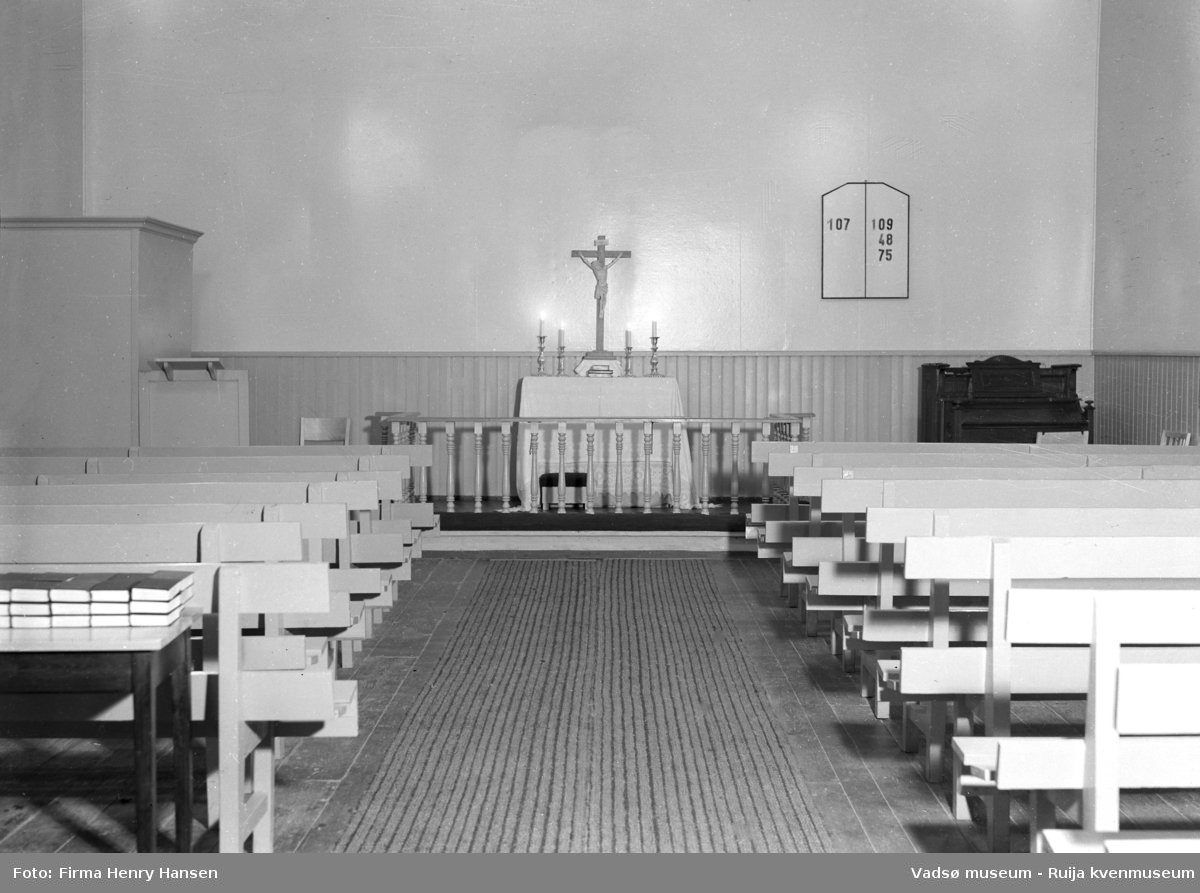 Vadsø interimkirke fotografert innvending, 1948. Fotografiet er av midtgangen med kirkebenker, alter, prekestol, orgel og salmetavle på endeveggen. Bedehuset fungerte i perioden mellom den gamle kirken brant til den nye kirken sto ferdig, som interimkirke( fra 1944 til 1958).