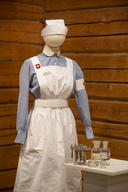 Sykepleieruniform på en dukke, med utstyr på et bord ved siden av.