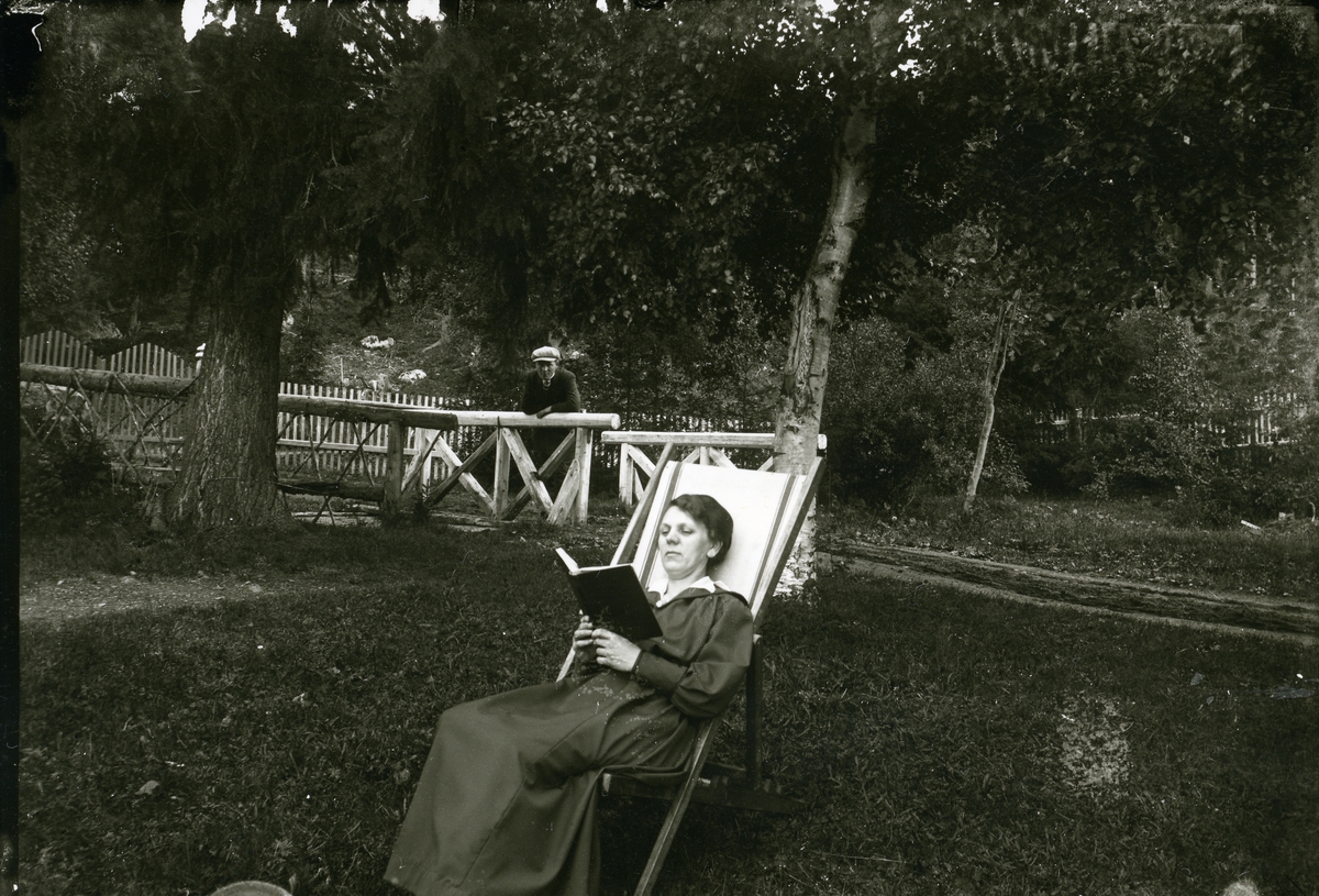 Kvinne i lenestol. Ein mann i bakgrunnen, ca 1910-1915.