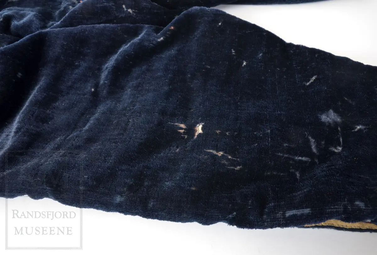 Mørk blå fløyelsbukse, knelang, med lem. Foret i lin. Fem flate messingknapper.